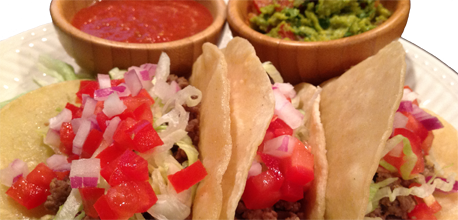 Three ground beef tacos served with salsa and guacamole.
